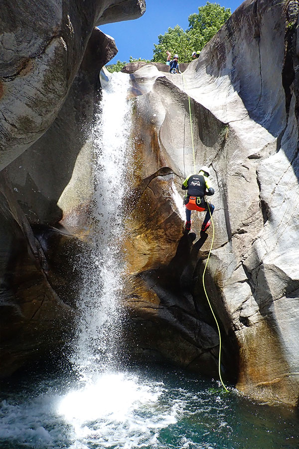 Teilnehmer seilt sich an einer hohen Felswand neben einem Wasserfall in Cresciano ab – geführte Canyoning-Tour mit purelements® im Tessin