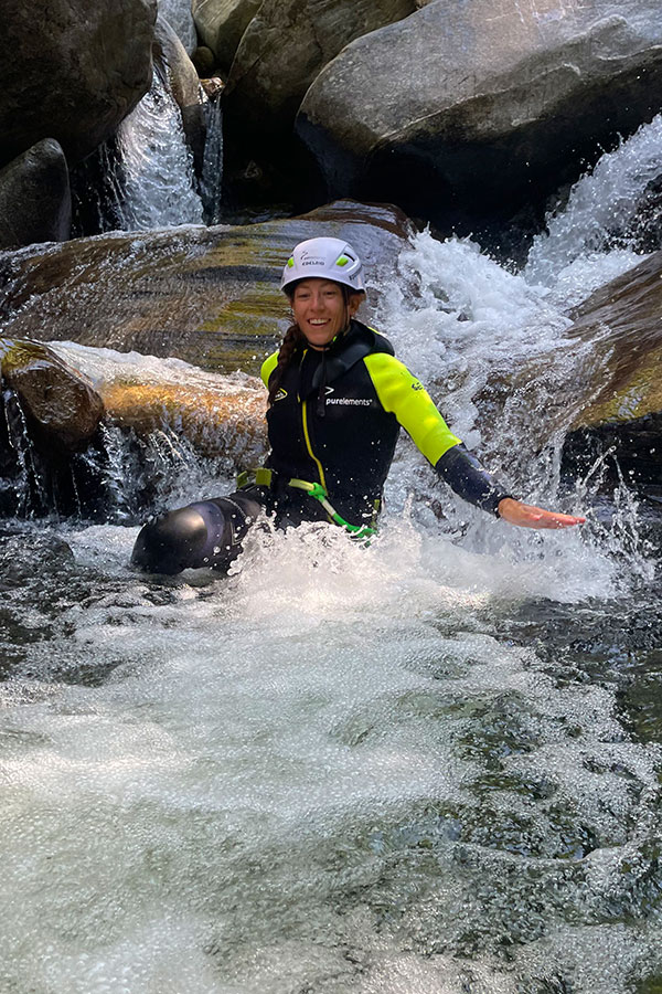 Teilnehmerin rutscht lachend eine natürliche Wasserrinne im Val Grande Canyon hinunter – Canyoning mit purelements® im Tessin