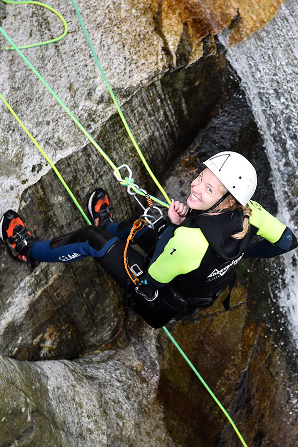 Donna sorridente che scende in corda doppia da una cascata - Vacanze avventura in Svizzera