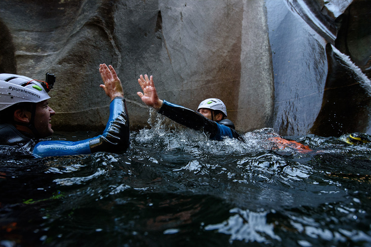 Zwei Canyoning-Teilnehmer geben sich ein High-Five im Wasser einer Schlucht im Tessin – purelements Canyoning Tour Schweiz